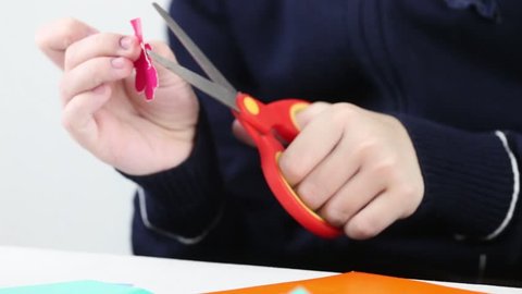 Hands of girl cutting flower from colored paper for crafts, closeup
