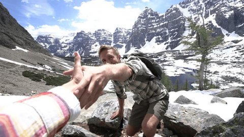 Young man hiking in the Canadian rockies, hand reach out to help. Helping hand, couple hiking, reach mountain top hand reaches out for assistance 