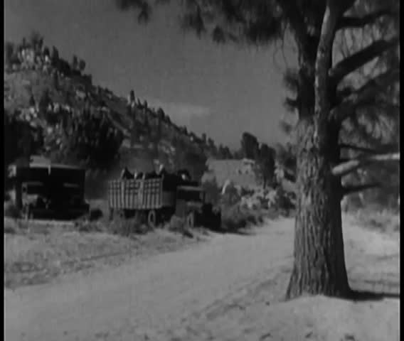 Wide shot of cars overtaking trucks on a dirt road