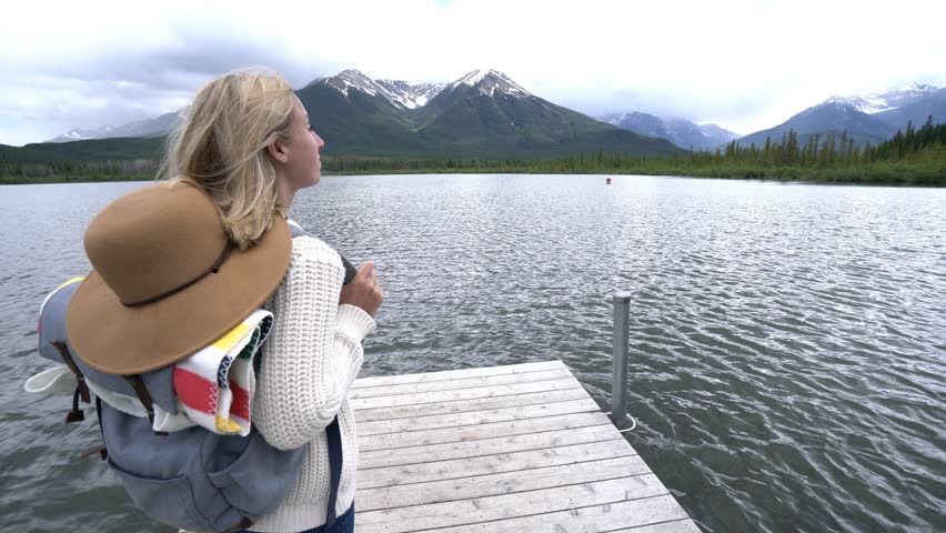 Woman standing on beautiful mountain lake looking at the stunning scenery of the Canadian rockies.
Woman contemplating nature