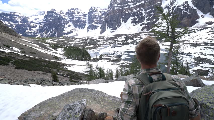 Man hiker relaxes on top of rock after reaching mountain peak. Young hiker contemplating nature from mountain top, stunning Canadian rockies scenery 