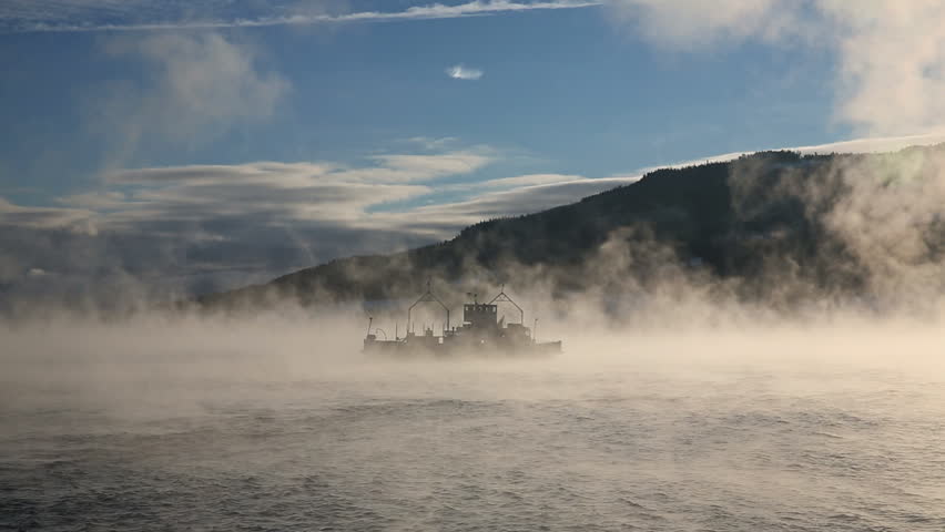 Ferry crossing fjord in sea smoke very cold weather condition