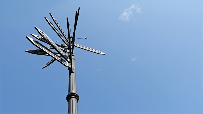 Low view of sign with european cities, young woman looking at them