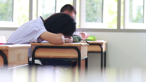 Asian Girl Student tired, lazy boring and sleeping on table during lecture at high school in exams classroom, education  overworking concept.
