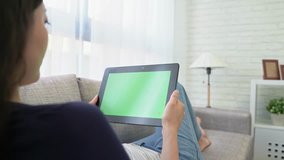 beautiful young woman is using a digital tablet and talking with green screen while sitting on sofa at home.