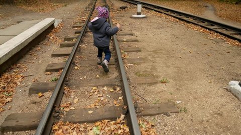 A little girl is walking on rails. Autumn forest