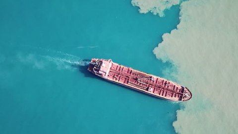 Dramatic Aerial top down shot of red deck tanker ship sailing on open sea with pollution 