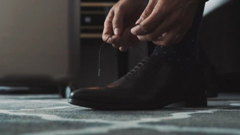 Unrecognizable businessman dressing up in a hotel room. Man tying his shoelaces. Close up. Slow motion.