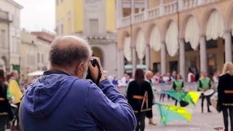 Man making photo and video during show flags thrower in European city Faenza in Italy back view. People looking holiday show on urban square: stockvideo
