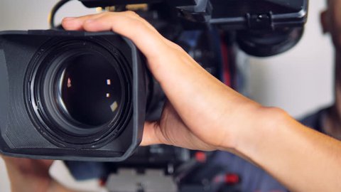 Male hands hold and move a large professional video camera in a close-up view. 