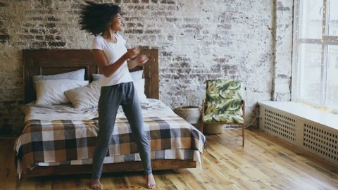 Attractive mixed race joyful girl have fun dancing near bed at modern apartment