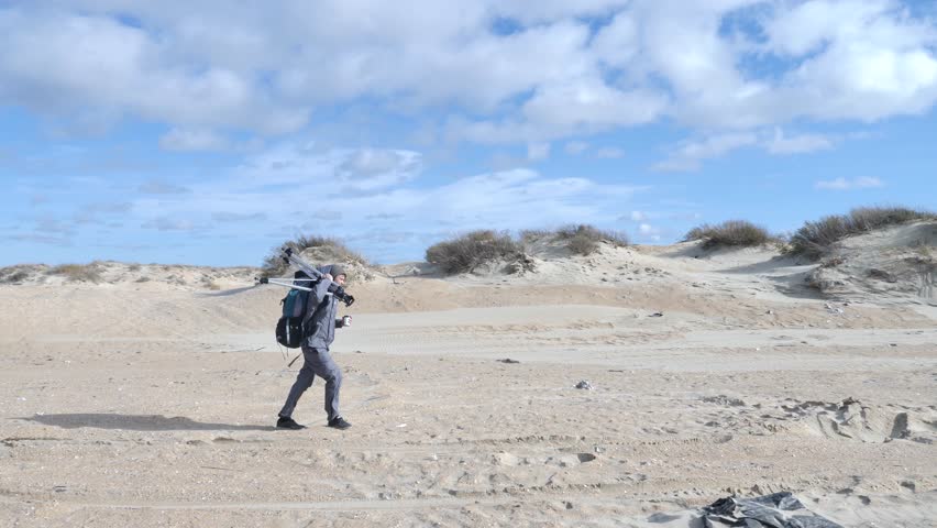 4k, professional photographer, hiker, walks in the desert with a tripod and a backpack to take pictures of the sea coast..