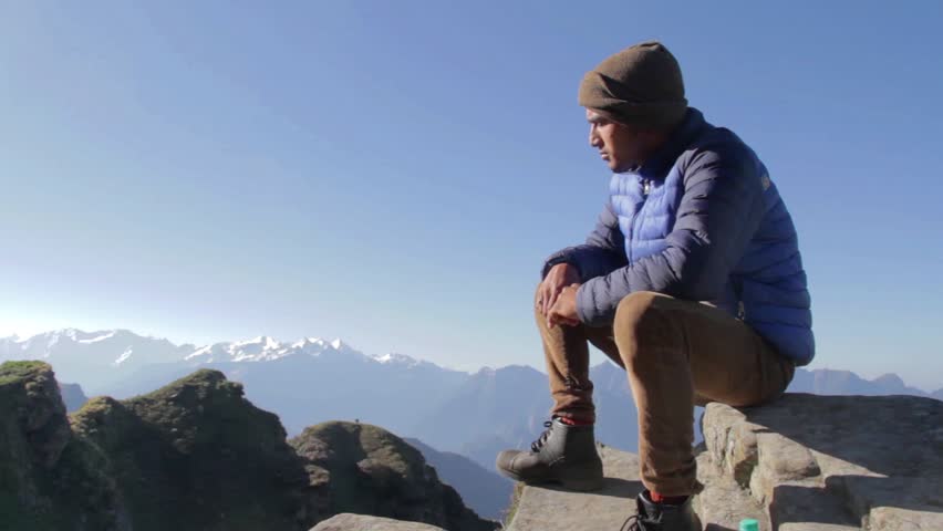 Optimistic young man sitting on the mountain summit