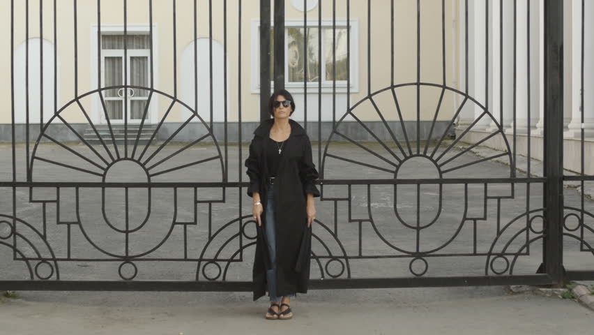 Beautiful young woman in sunglasses leaning on metal gate.