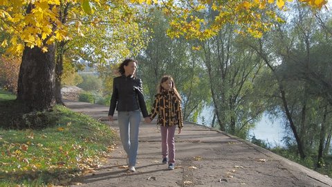 A happy family walks through the autumn park. Mother and daughter are walking along the embankment.