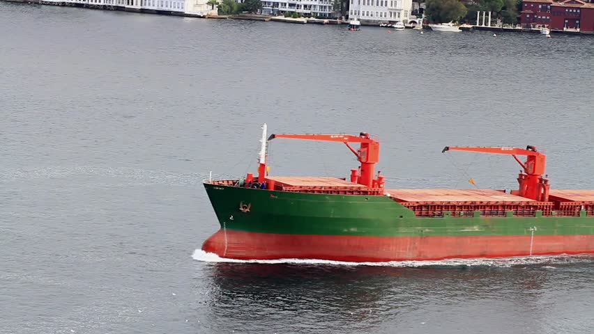Green cargo ship with deck cranes sailing in straits flowing water. A 115 mt