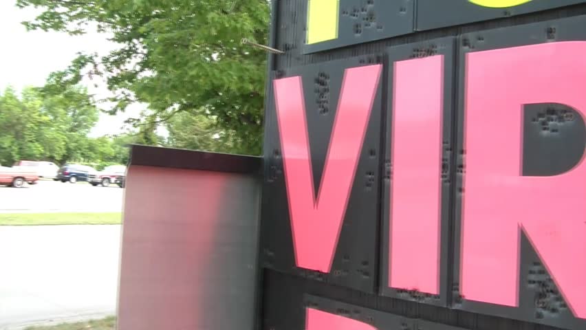 Pan from left to right of virus removal sign in bright pink lettering on roadside in natural light.