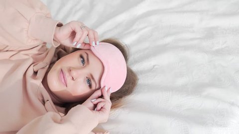 Woman wears sleep mask in the bed, attractive pretty caucasian woman yawns in the bed, the girl is stretching, preparation for sleep, daytime sleep and relaxation