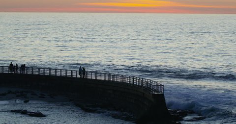 Slow motion of tourists walking at sunset on the seawall at Children's Pool, La Jolla, California.