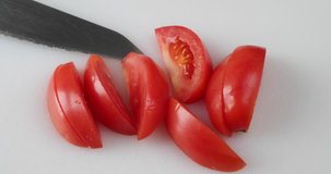 Sections of a ripe red roma tomato being placed on a white plate atop a cutting board.
