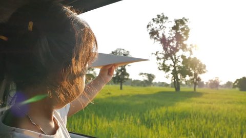 Cute little girl having fun to play with toy paper aircraft out of car window in the countryside. Concept of activity relaxing in evening. Slowmotion shot