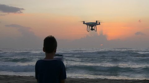 Boy operating a drone with remote control.  Quadro copter drone flying over sunset sea. 4K, UHD Video Stok
