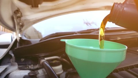 Super slow motion Pouring fresh new clean synthetic oil into car's engine, closeup.