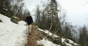 Hiker man with backpack walking on snowy trail path.Following front.Real backpacker people adult hiking or trekking in autumn or winter in wild mountain outdoors nature,bad foggy weather.4k video