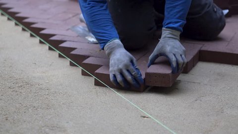Man putting red brick pavers into place in a herringbone pattern on a bed 