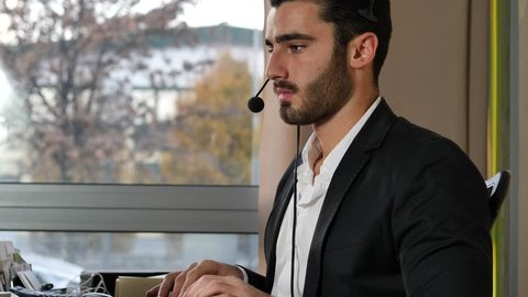 Good looking young man with headset working as help-desk assistant, customer service, help-line or telemarketer in office