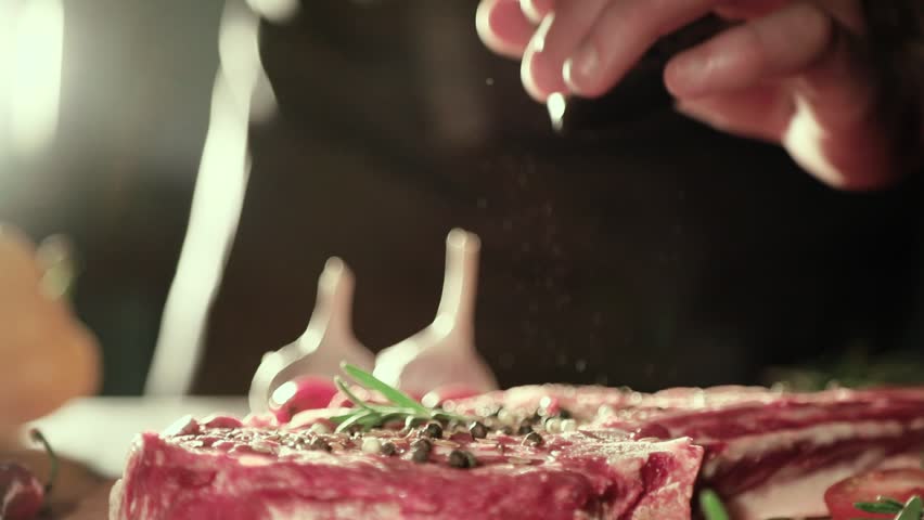 Close Up of Chef’s Hand Seasoning Fresh steak in a Bright Light. Chief added spices to beef steak. Italian Cuisine, Bon Apetite, Fresh Meat, Pepper Salt, Garlic and Rosemary Royalty-Free Stock Footage #32709055