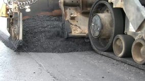 Clip of heavy equipment asphalt laying machine dropping blacktop tar onto new parking lot for school.