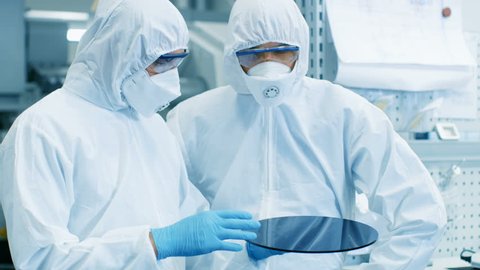 Two Engineers/ Scientists/ Technicians in Sterile Suits Check Semiconductor Silicon Wafer. They Work in a Modern Semiconductor Fabrication Plant. Shot on RED EPIC-W 8K Helium Cinema Camera.