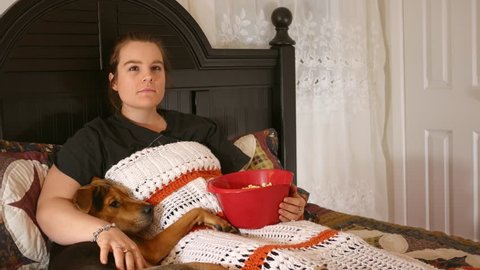Content Woman watches a movie in bed while cuddling with a puppy