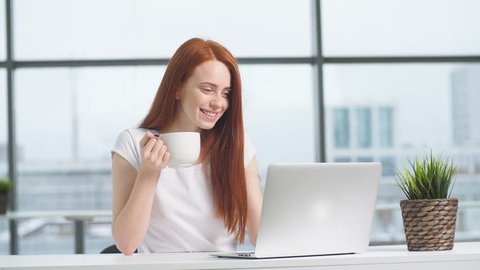 Happy redhead girl working at laptop in office.