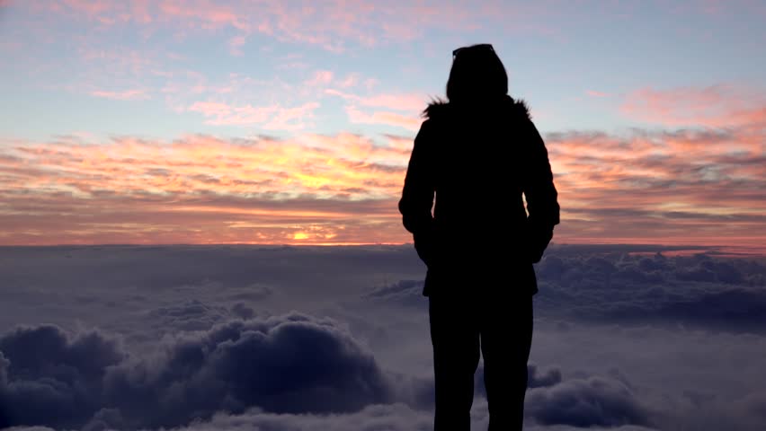 Girl enjoy amber sunset over clouds at the summit of Haleakala (East Maui Volcano). Haleakala NP, Maui, Hawaii, USA