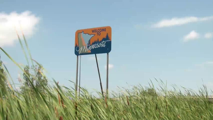 Small blue welcome to Minnesota sign lining a highway leaving North Dakota on side of highway.