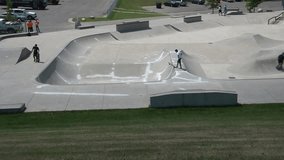 Clip of concrete skateboard park with riders doing tricks, shot from an aerial view atop a hill.
