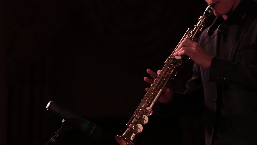 A man in a black suit plays music on soprano saxophone on a dark background of the stage. Royalty-Free Stock Footage #32729899