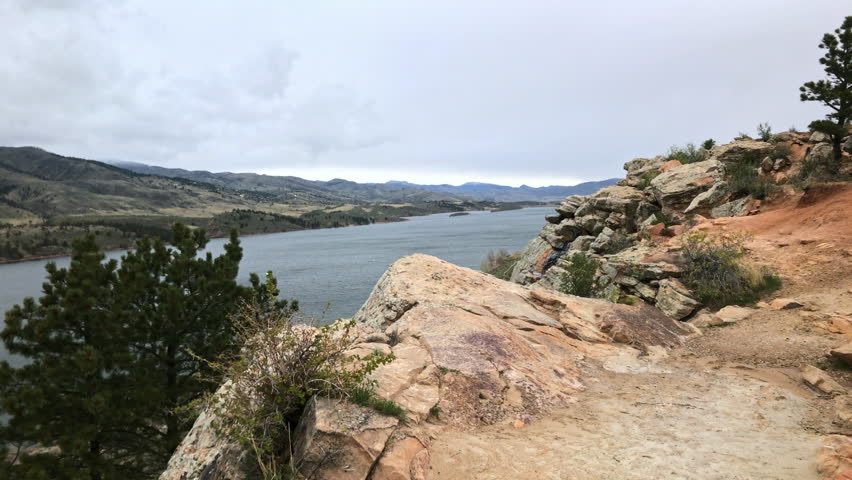 A pan from the trail to the mountains and Horsetooth Reservoir overlook, as a dog comes in and out of frame.