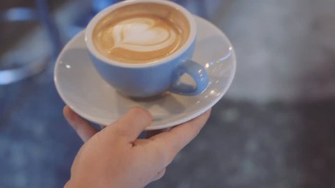 Camera follows waiter who carries fresh and perfectly made coffee with latte art on top, made out of fresh and organic fairtrade beans, through cafe or bar to satisfied customer at big table