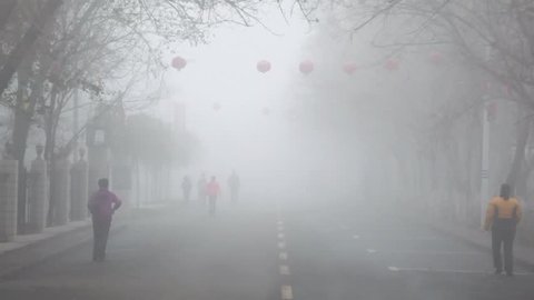 People walk by street covered by fog at autumn morning