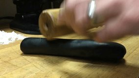 Squid ink pasta being rolled out with a wooden rolling pin with flour in background.  