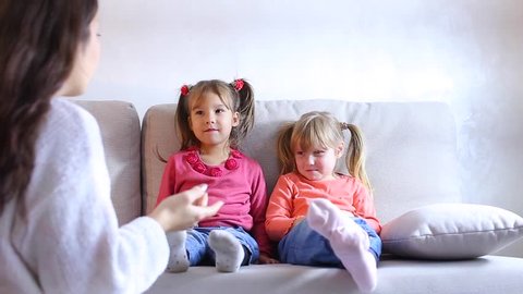 Two small girls sit on couch in living room and cry, children do not want to go to kindergarten. Mom tells daughters to gather in kindergarten, children upset and begin to cry. Daughters dressed in