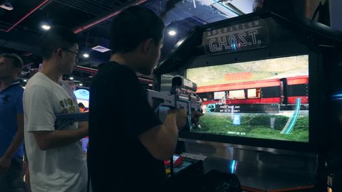 Young Mixed Race Friends Playing Arcade Shooter Game Machine in Game Zone MBK Shopping Center. 4K. Bangkok, Thailand - 15 NOV 2017.