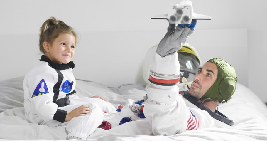 Romantic and family moments of dad and daughter playing with spacecraft, both dressed as astronauts and are happy at this unique moment. Concept of: love, family, home, games.