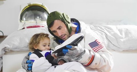Romantic and family moments of dad and daughter playing with spacecraft, both dressed as astronauts and are happy at this unique moment. Concept of: love, family, home, games.