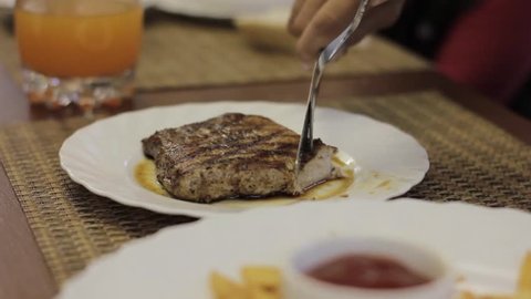 Cutting roast beef on a white plate, teenager eats meat in a cafe