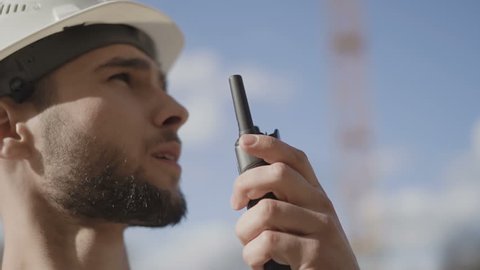 Engineer builder using a walkie talkie giving instructions at a construction site. Slow motion