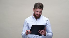 Happy bearded man in shirt writing something in documents and showing ok sign over gray background